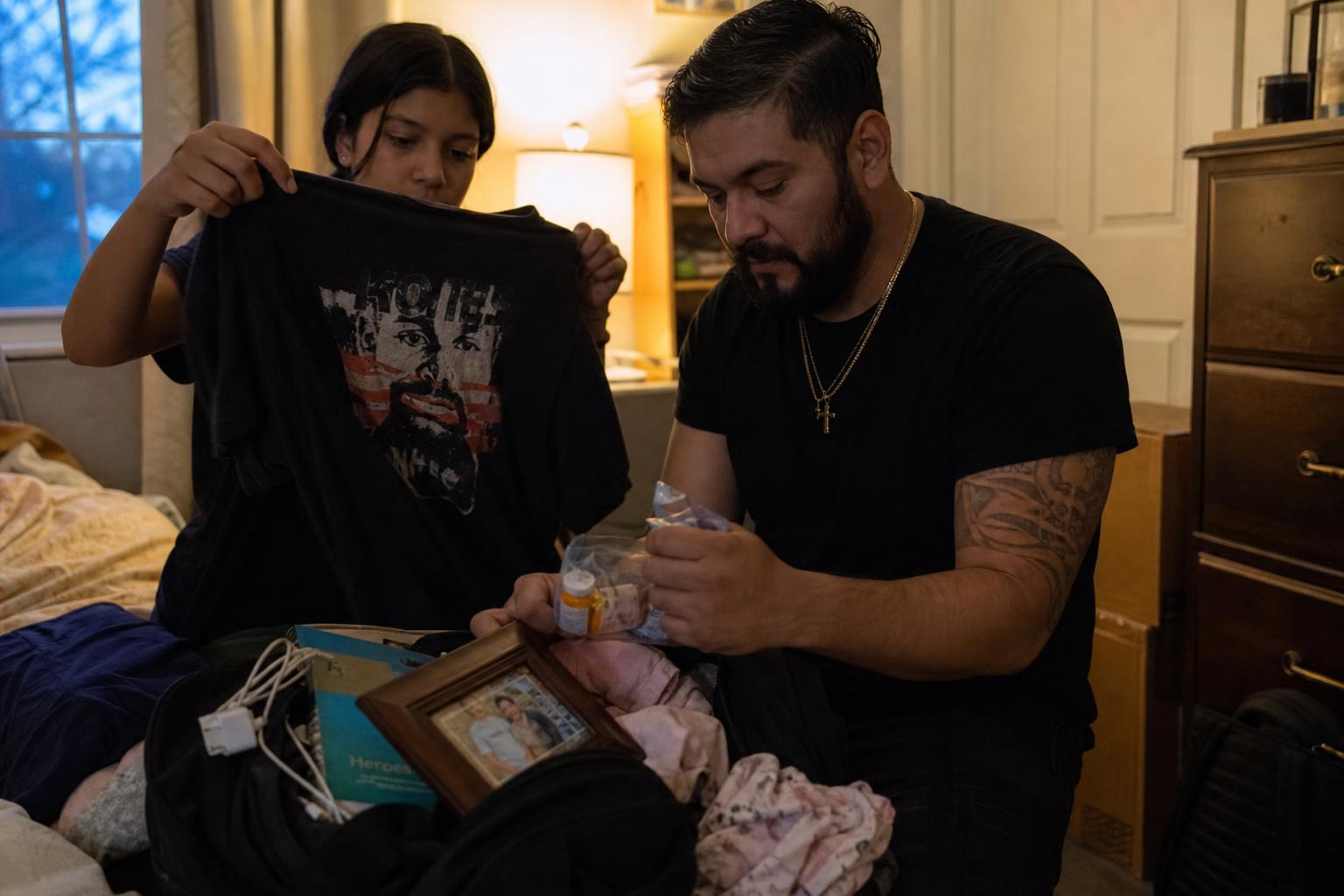 A young Latino single father and his teenage daughter packing an overnight hospital bag together in warm light.
